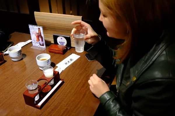 Visitor enjoying a sake tasting flight in small cups at Kizakura's tasting bar in Fushimi, Kyoto