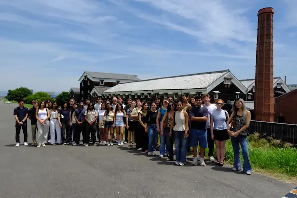 U.S. university student group photo in front of Matsumoto Sake Brewery's historic building and red-brick chimney in Fushimi, Kyoto