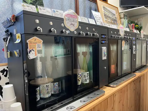 Self-serve sake tasting dispensers at Sasaki Sake Brewery's shop, with bottles of Jurakudai and other Kyoto sake