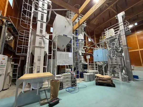 Inside Matsumoto Sake Brewery's in-house rice polishing facility, showing tall industrial milling equipment