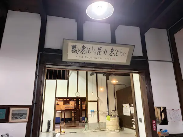 Calligraphy sign inside Matsumoto Sake Brewery reading "the brewery may age, but never let the interior grow old," the brewery's guiding motto